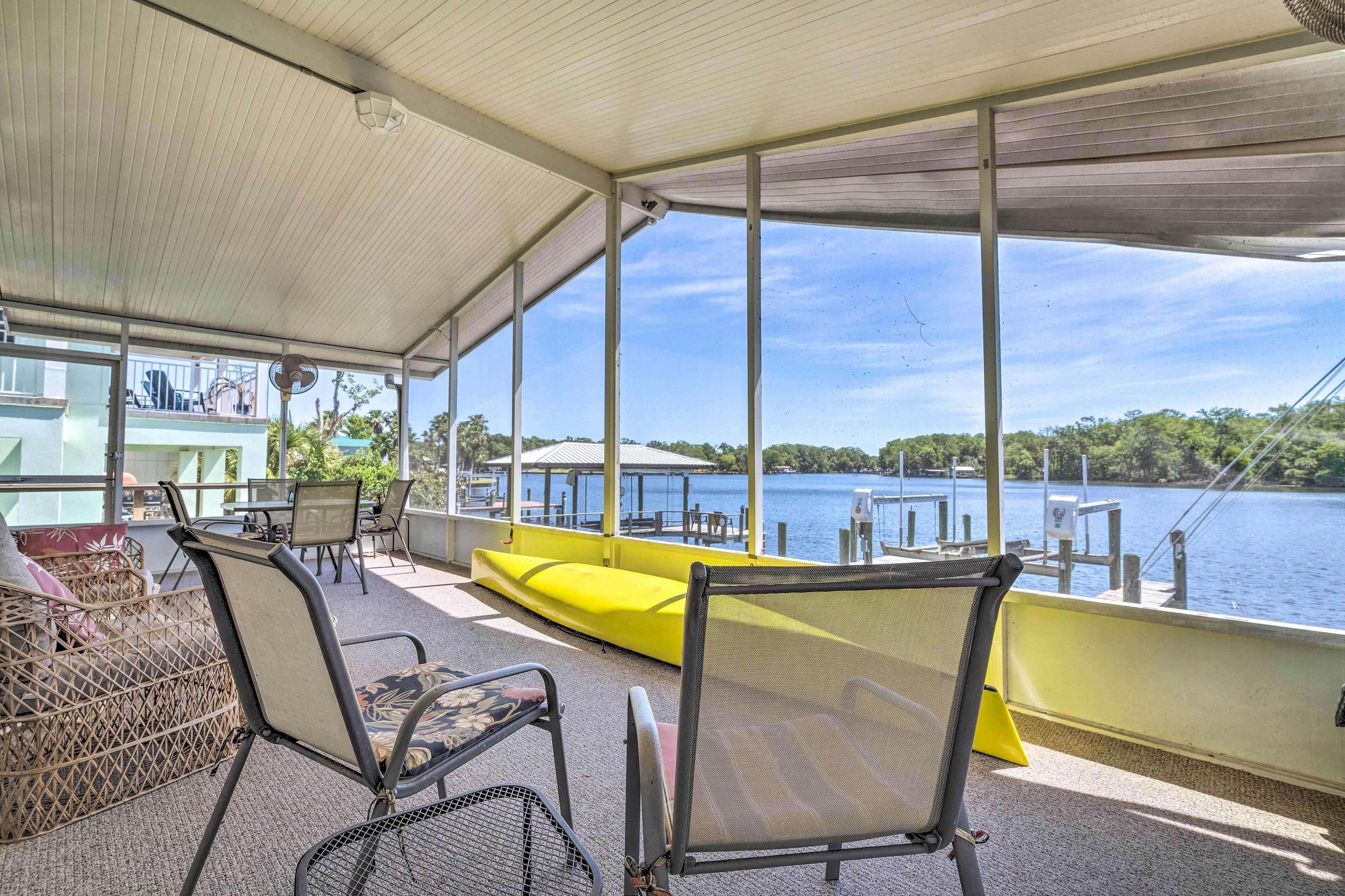 Un espace extérieur abrité, aménagé avec des chaises et un banc jaune, qui offre une vue sur un lac avec des quais et de la végétation.