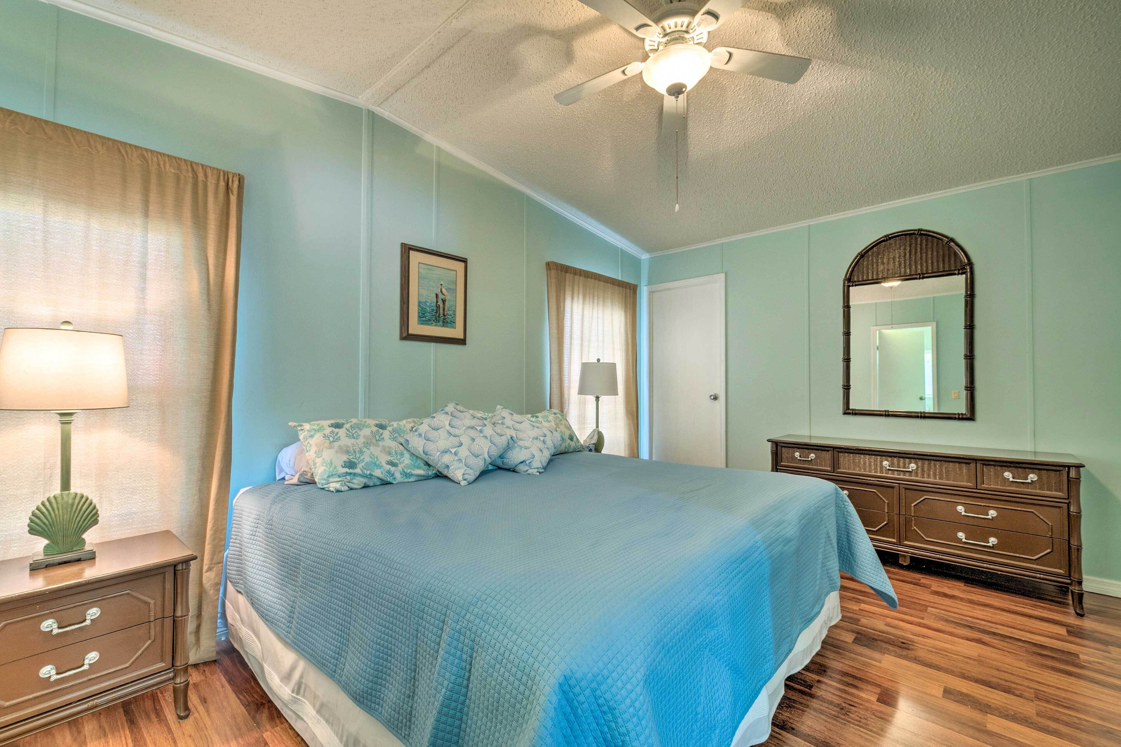 A bedroom with a bed, a dresser, a nightstand, a ceiling fan, and a mirror.