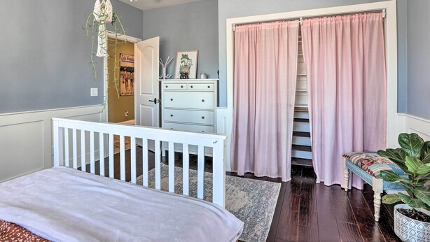 Une chambre avec un berceau, une commode, un banc et un escalier, le tout agrémenté de rideaux roses.