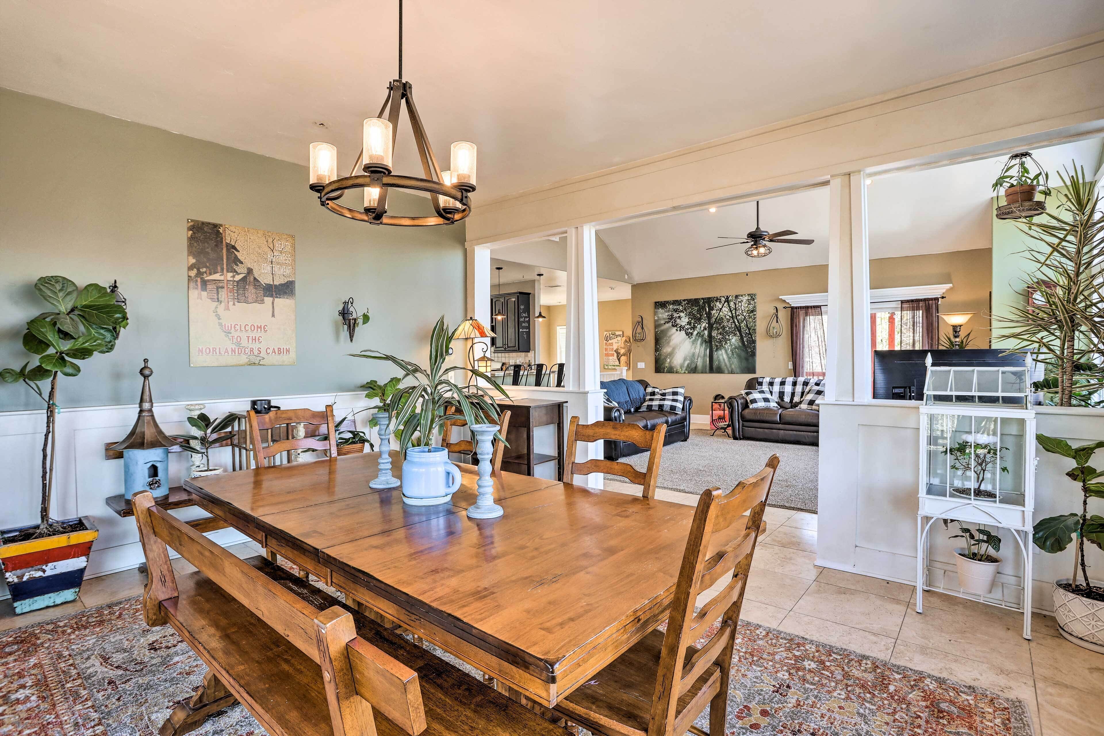 A spacious dining area with a wooden table and chairs, surrounded by potted plants and a chandelier.