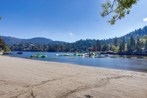 A beach with kayaks and rafts, a sandy shore, and a forested hillside in the background.
