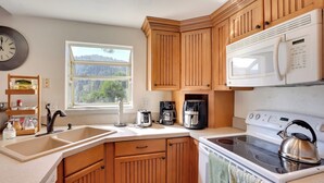 A kitchen with wooden cabinets, a white microwave, a stove, and a coffee maker. - Lake & Mountain-view Home: Walk to Downtown! (Crestline)