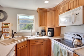 A kitchen with wooden cabinets, a white microwave, a stove, and a coffee maker. - Lake & Mountain-view Home: Walk to Downtown! (Crestline)