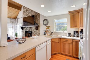 A kitchen with wooden cabinets, a stone wall, a clock, and a dishwasher.