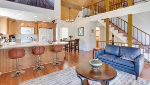 A spacious living area with a blue sofa, a coffee table, and a kitchen with wooden cabinets and a white refrigerator. - Lake & Mountain-view Home: Walk to Downtown! (Crestline)