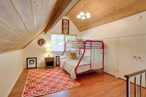 A dormitory room with a bunk bed, wooden flooring, a red and white patterned rug, a desk with a lamp, a framed picture, and a window with blinds. - Lake & Mountain-view Home: Walk to Downtown! (Crestline)