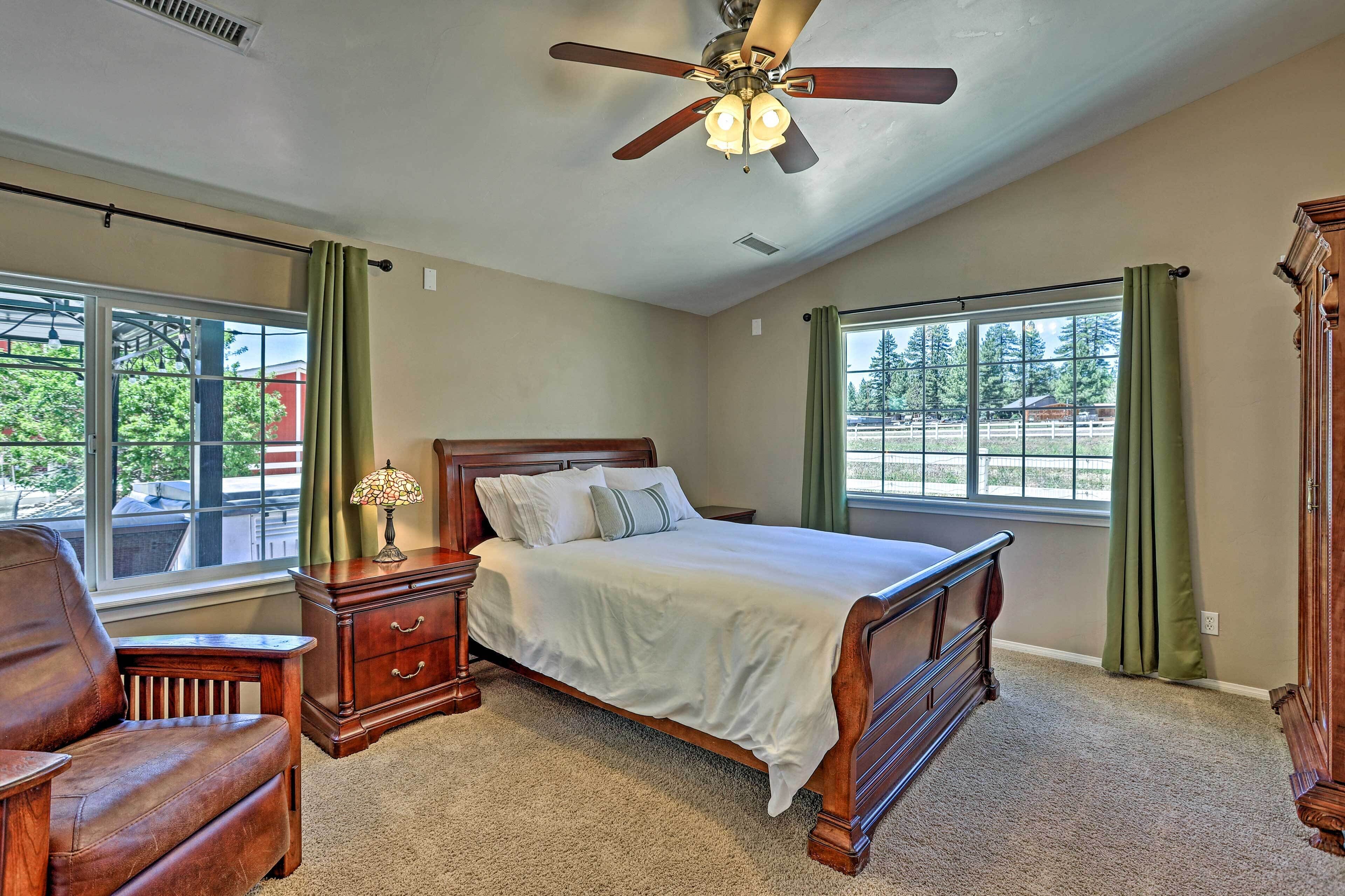A bedroom with a large bed, a wooden nightstand, a leather chair, and a ceiling fan.