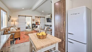 A compact kitchen with a wooden table, a bowl of fruit, and a white refrigerator. - Modern Joshua Tree Bungalow With Fire Pit & Bbq! (Joshua Tree)