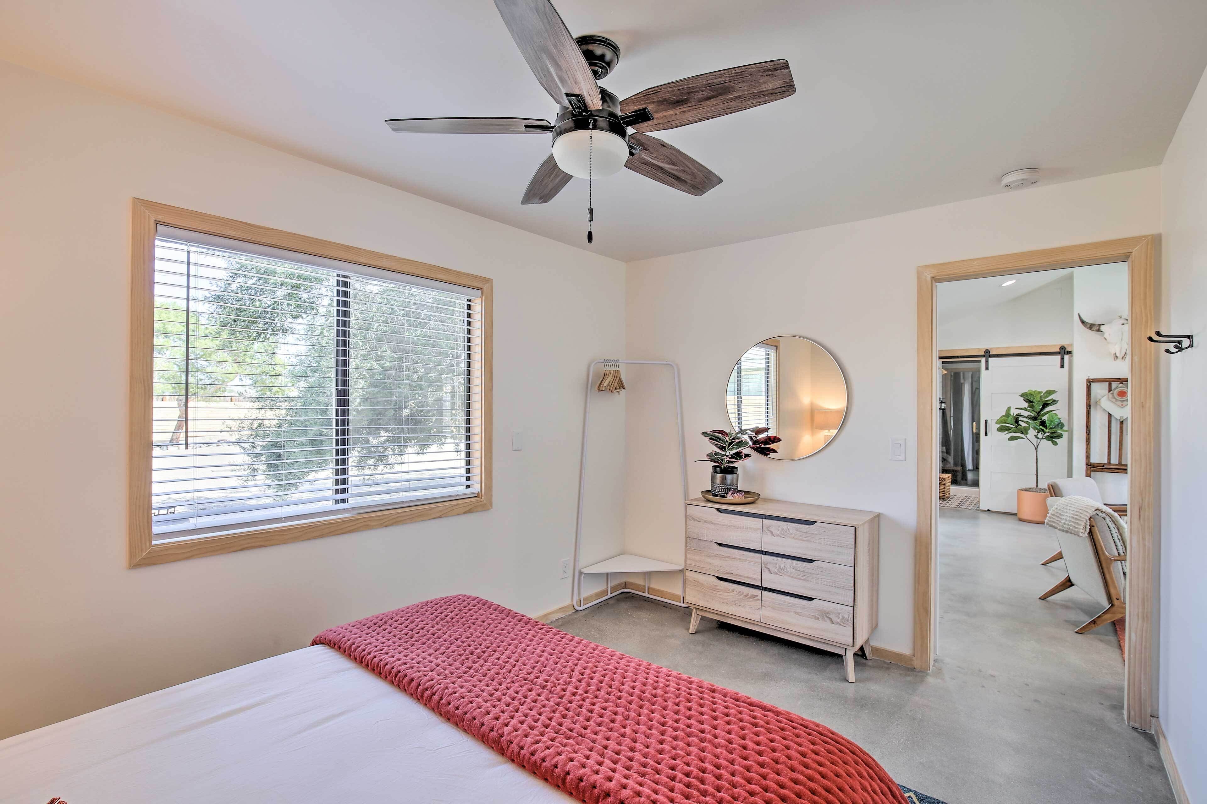 A bedroom with a bed, a ceiling fan, a dresser, a mirror, and a window with blinds.