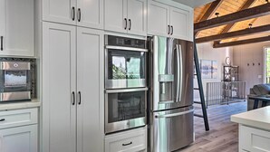 Une cuisine moderne dotée d’appareils électroménagers en acier inoxydable, de meubles blancs et d’un plafond en bois.