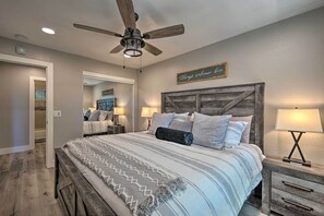 Une chambre à coucher avec un grand lit, un ventilateur de plafond, une tête de lit en bois et une table de chevet avec une lampe.