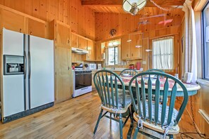 A wooden cabin kitchen with a refrigerator, stove, and dining table with chairs. - Big Bear Lake Cabin w/ Deck ~ 7 Mi to Ski Slopes! (Fawnskin)