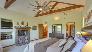 A spacious bedroom with a large bed, a fireplace, a ceiling fan, and a television on a shelf. - Luxe Lake Arrowhead Home w/ Deck, 3 Mi to Village! (Lake Arrowhead)