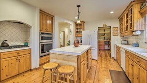A kitchen with wooden cabinets, a central island with stools, a refrigerator, oven, and a hanging light fixture. - Luxe Lake Arrowhead Home w/ Deck, 3 Mi to Village! (Lake Arrowhead)