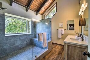 Ein modernes Badezimmer mit einer Glaskabine zur Dusche, einem großen Fenster und einer Holzbeschichtung der Decke.