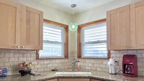 A kitchen with wooden cabinets, a granite countertop, a sink, a coffee maker, and a window with blinds. - IslandSeabreeze-Steps to Beach+1 Night Stays+Great for Cruisers/Families/Couples (Galveston)
