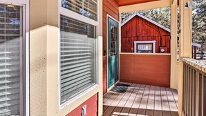 A covered porch with a red barn-like structure, a door, and a window with blinds. - 5 Mi to Big Bear Lake: Cozy Cottage w/ Hot Tub (Big Bear City)