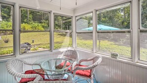 A sunroom with wicker chairs and a glass table, large windows with a view of a garden and a blue umbrella. - Stockbridge Home: Walk to Town Beach! (Stockbridge)