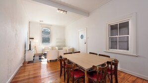 A spacious dining room with a wooden table and chairs, a white sofa, and a large window. - Private Unit in Heritage Building in Fitzroy North (Fitzroy North)