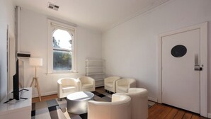 A modern living room with white furniture, a large window, and a checkered rug. - Private Unit in Heritage Building in Fitzroy North (Fitzroy North)