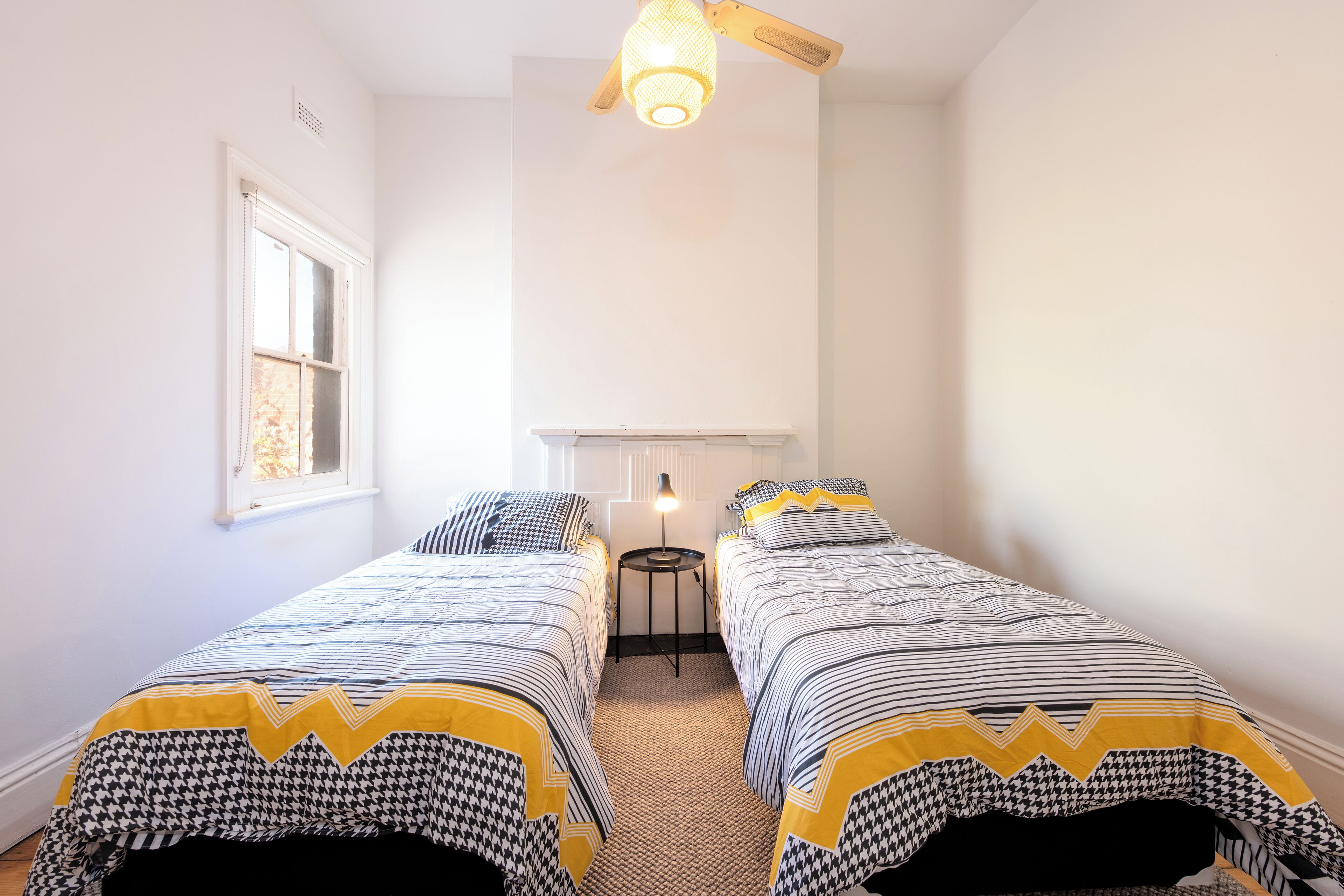 Une chambre avec deux lits simples, une petite table et un luminaire au plafond.