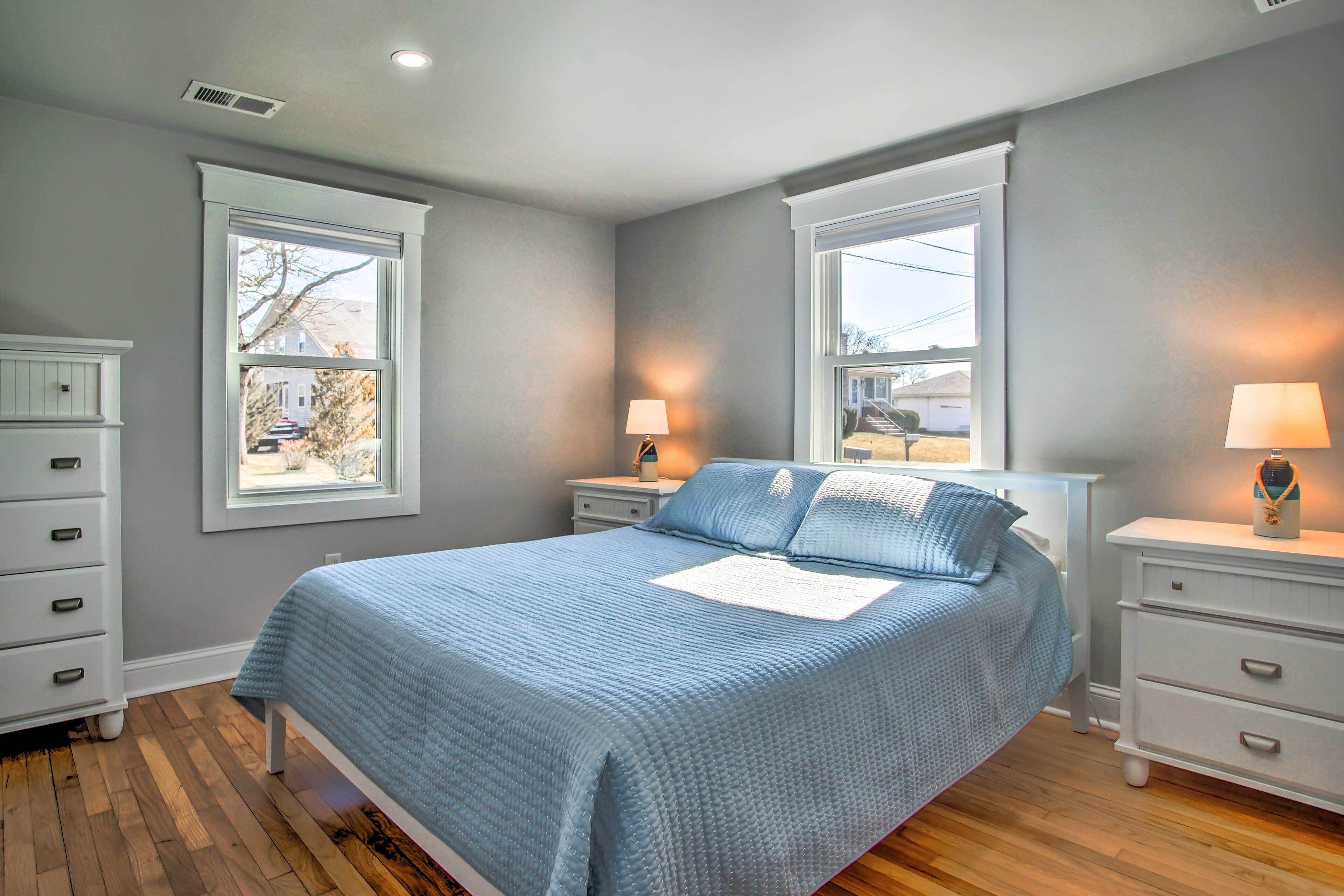 A bedroom with a bed, two nightstands, a dresser, and two windows.