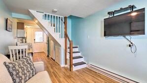 Un salon moderne avec un escalier, un téléviseur à écran plat fixé au mur et un coin repas à l’arrière-plan.