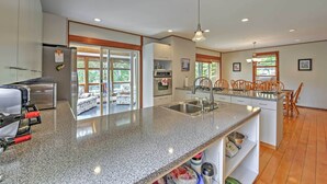A modern kitchen with granite countertops, stainless steel appliances, and a dining area with wooden chairs. - Walk to Beach! Hyannis Family Haven w/ Deck (Hyannis)