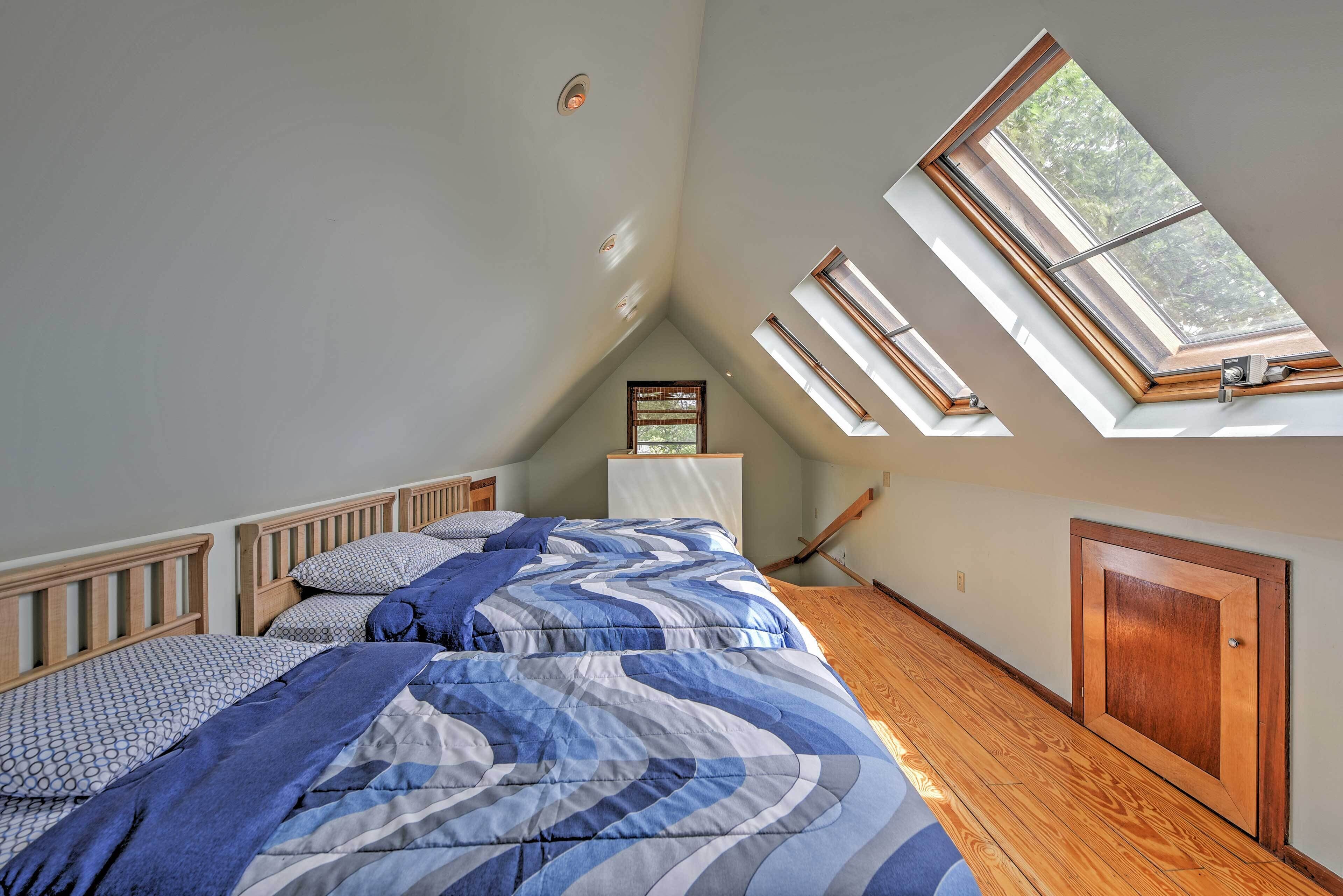 A bedroom with a sloped ceiling, skylights, wooden flooring, and a bed with blue bedding.