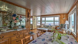 Interior d'una cabana de fusta amb taula de dinar, cadires, un sofà i vista al llac a través de grans finestres.
