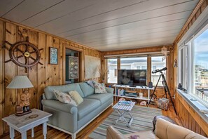 A cozy living room with a wooden interior, a sofa, a small table, a lamp, and a TV. - Deck & Beach Access: Waterfront Cape Cod Cottage (Wareham)