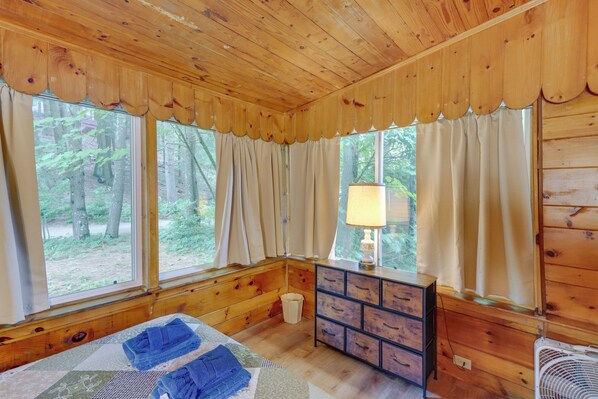 Una habitación tipo cabaña de madera con una cama, cómoda y ventanas con vistas a un bosque.