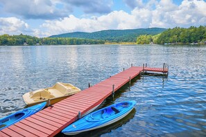 Un muelle de madera se extiende sobre aguas tranquilas, con kayaks y una canoa amarrados al final.