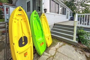 Trois kayaks sont garés devant une maison dotée d’un porche et d’un escalier menant à l’entrée.