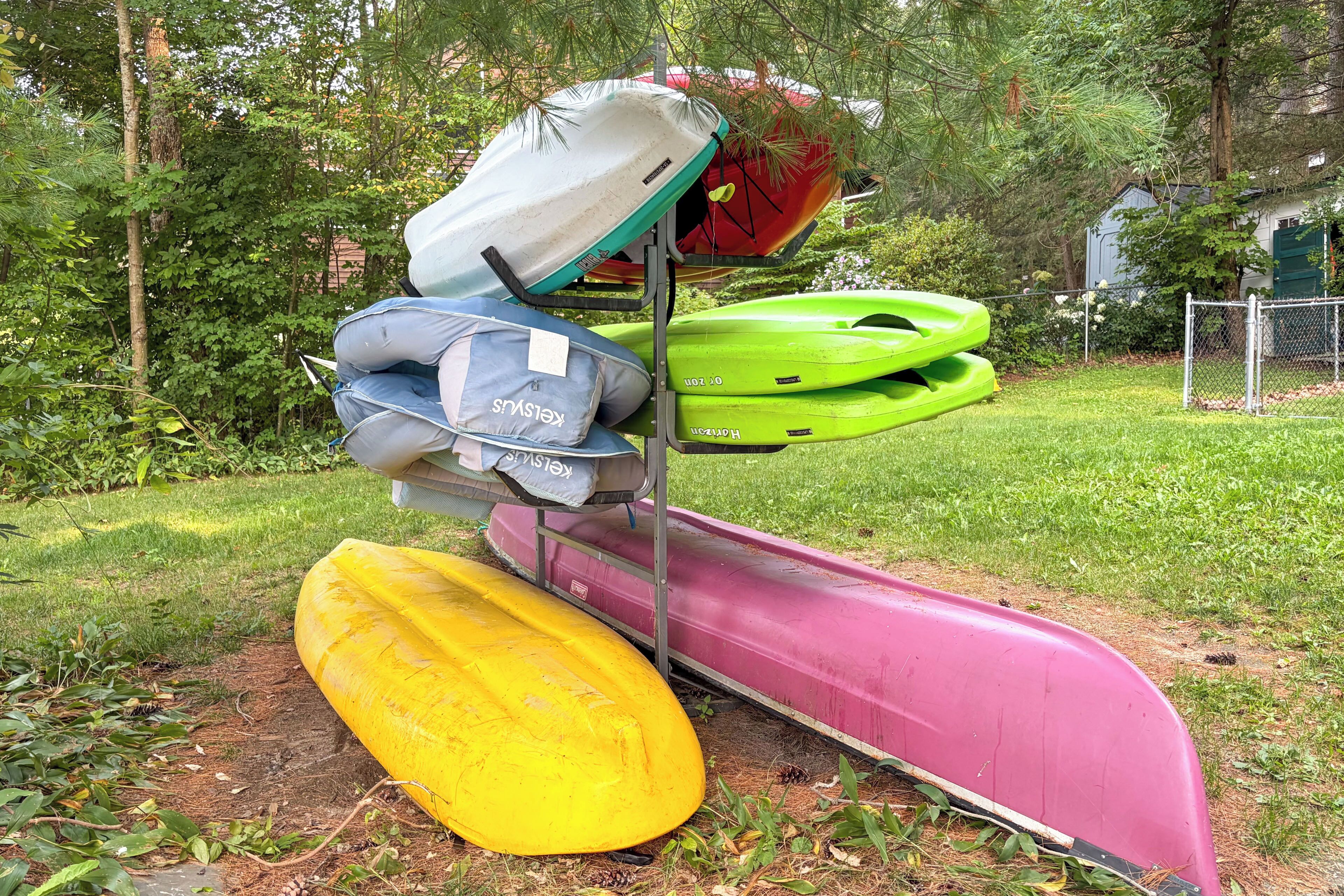 A metal rack holding kayaks and a paddleboard in a grassy outdoor area.