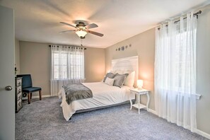 Un dormitorio con cama, ventilador de techo, mesita de noche, una silla y ventana con cortinas translúcidas.
