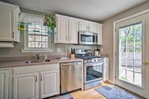 Una cocina con armarios blancos, electrodomésticos de acero inoxidable, un ventanal con vistas y una puerta que da al exterior.
