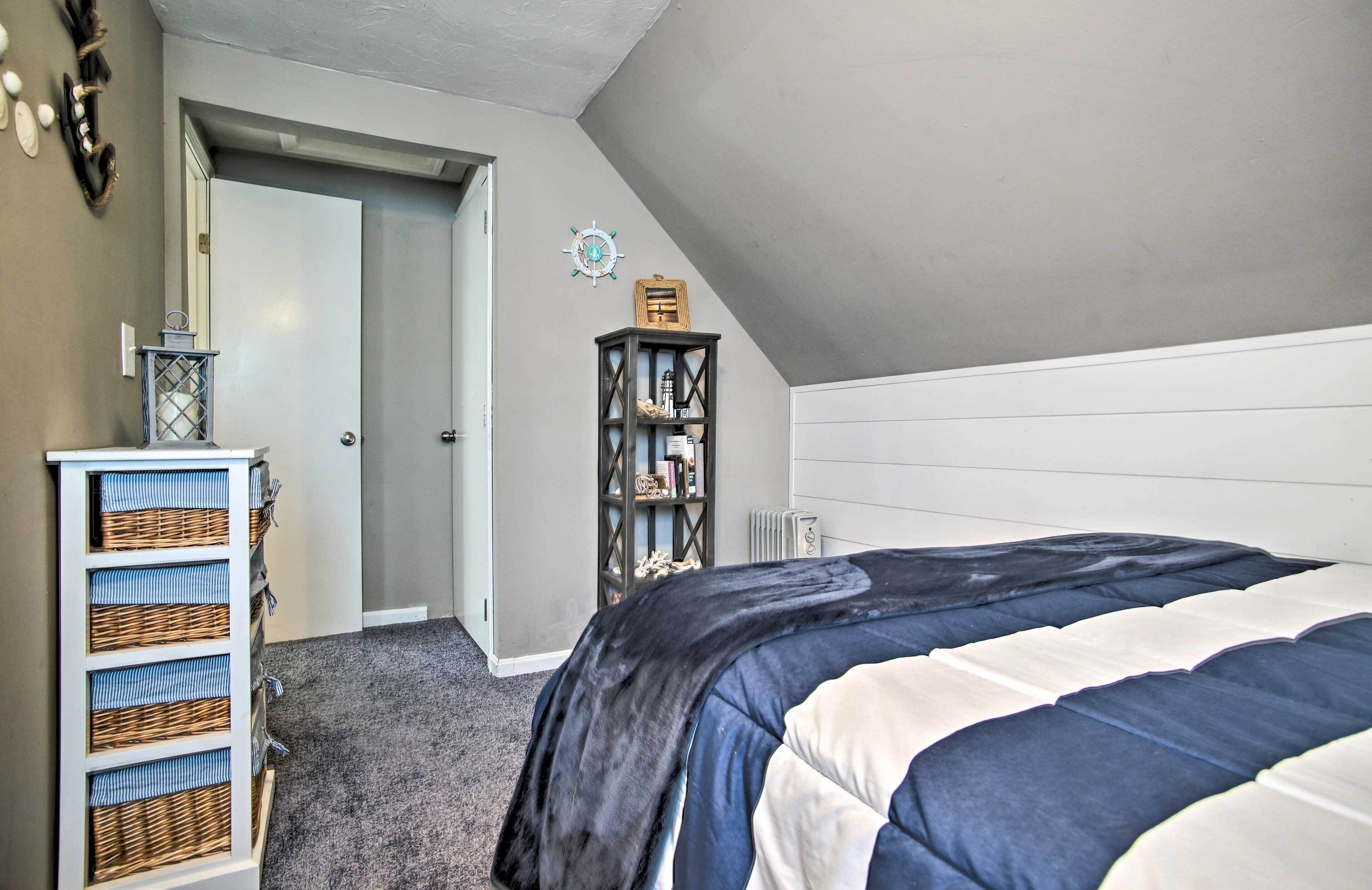 A bedroom with a bed, a dresser with baskets, a bookshelf, and a door leading to another room.