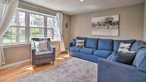 Een woonkamer met een blauwe bank, een grijze fauteuil en een raam met gordijnen.
