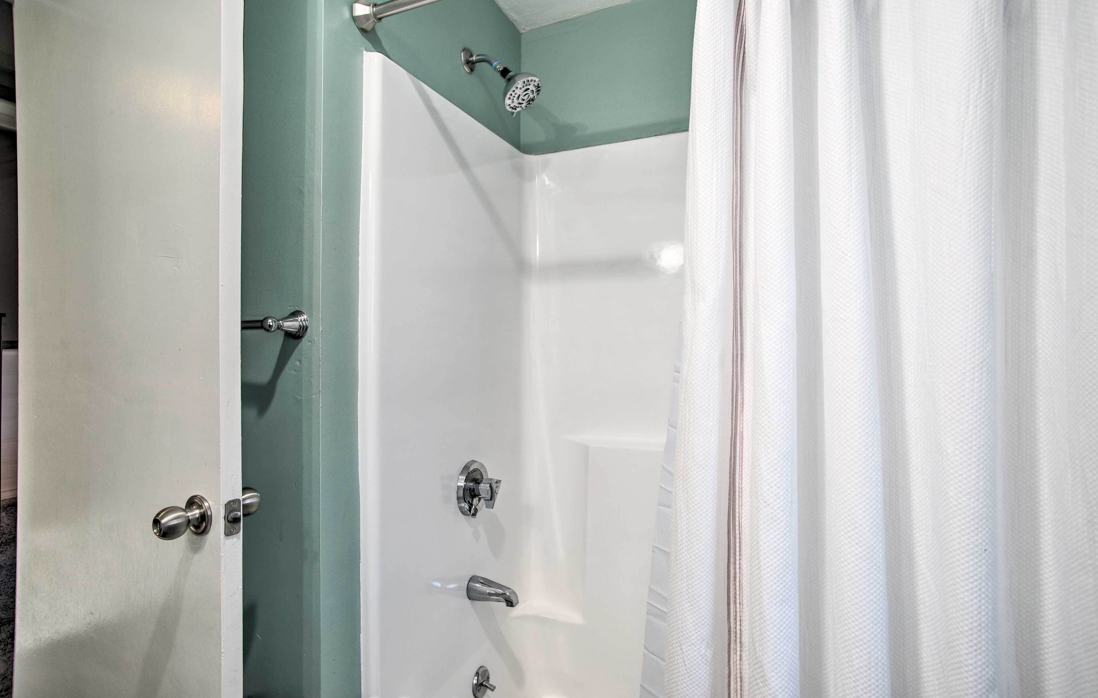 A bathroom with a shower, a door with a handle, and a curtain.