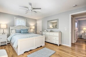 Un dormitorio con cama, mesitas de noche, cómoda, ventilador de techo y espejo.