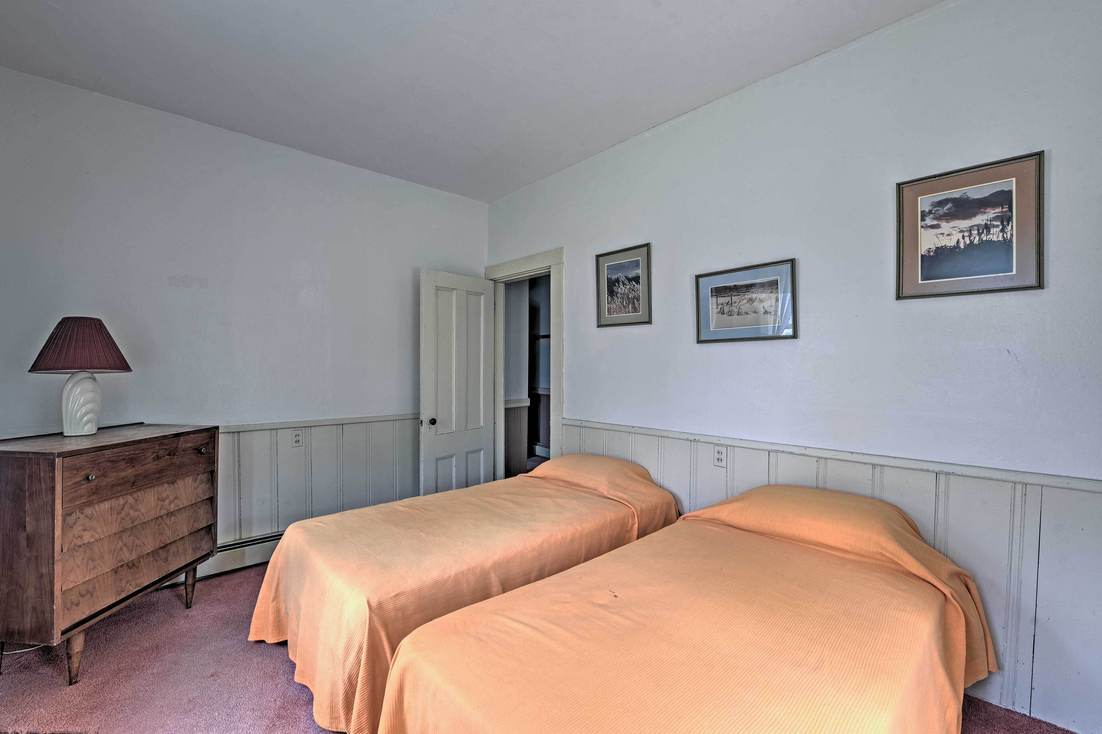 A bedroom with two single beds, a wooden dresser, and framed pictures on the wall.