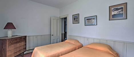 A bedroom with two single beds, a wooden dresser, and framed pictures on the wall.
