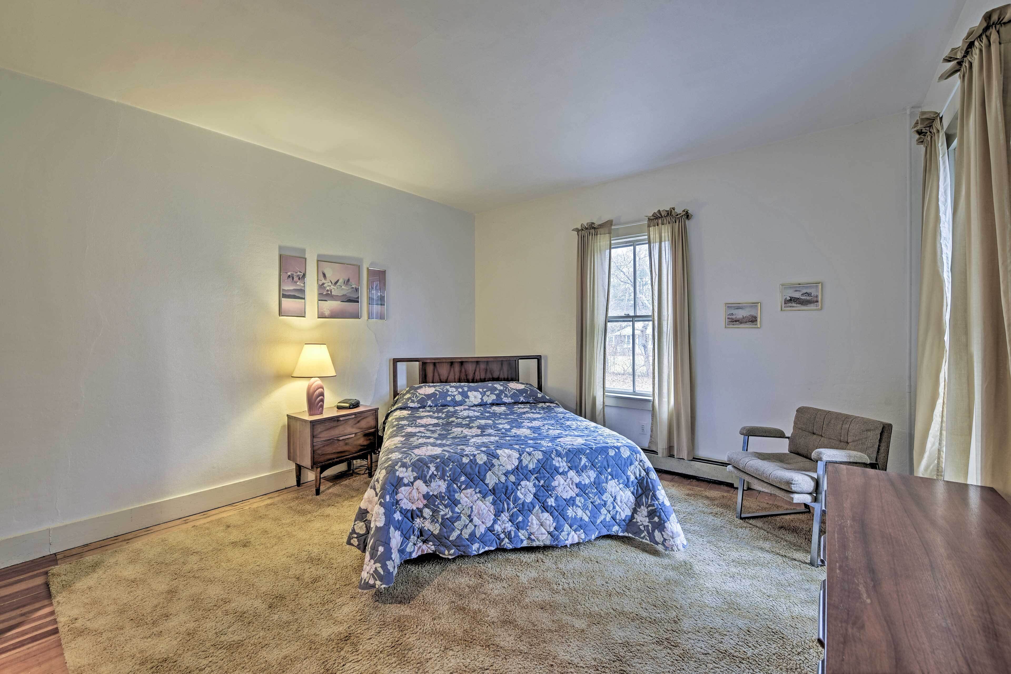 Une chambre à coucher avec un lit, une table de chevet, une chaise et une fenêtre avec des rideaux.