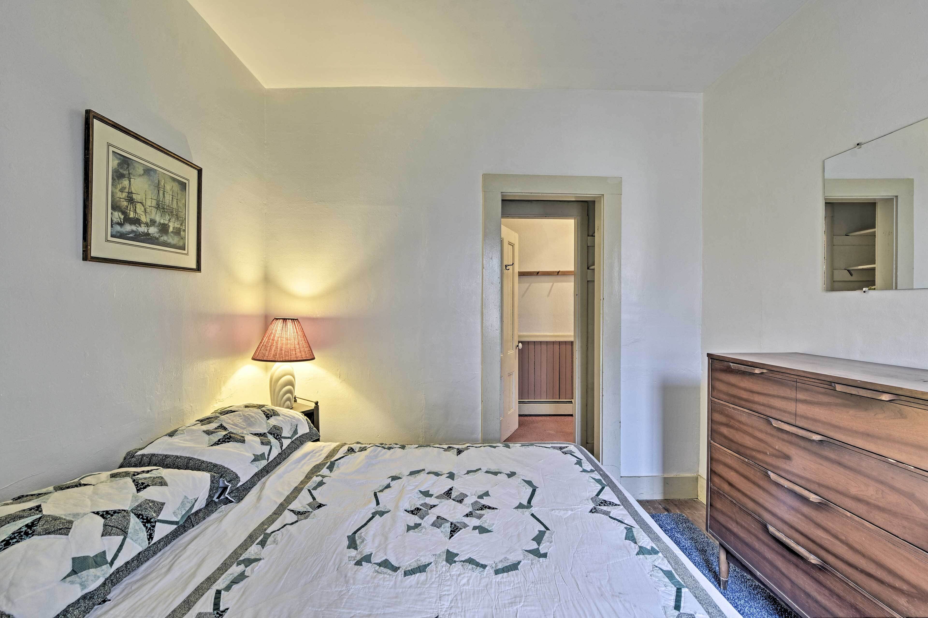 A bedroom with a bed, a dresser, a lamp, a framed picture, and a closet.