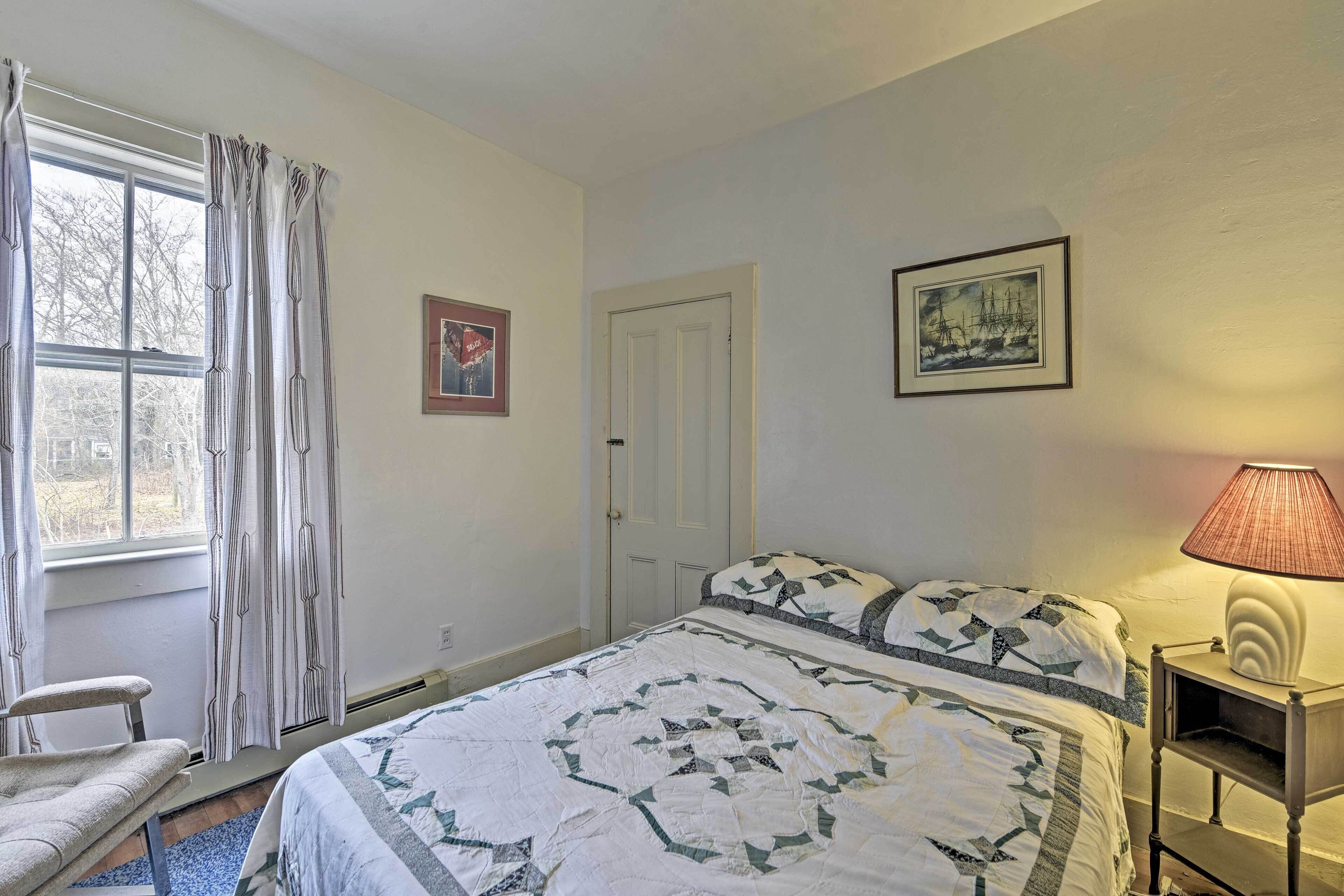 A bedroom with a bed, a chair, a window with curtains, a door, and a lamp on a bedside table.