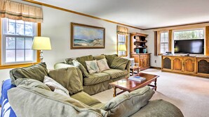 A living room with a green sofa set, a wooden cabinet, a television, and a painting on the wall. - 2 Mi to Shore: Home w/ BBQ & Beach Gear in Mashpee (Mashpee)