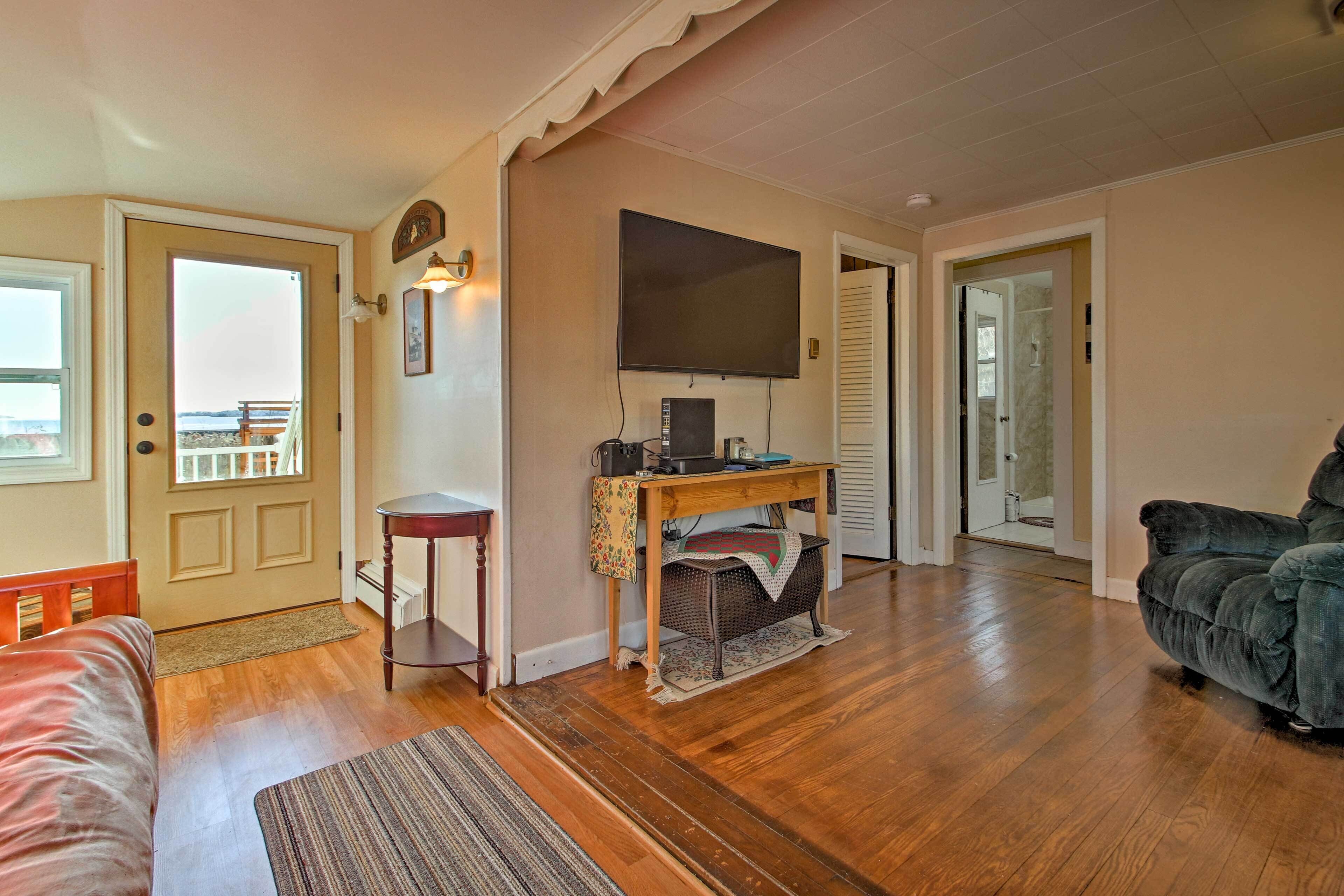 Un salon doté d’un parquet, d’un canapé, d’un téléviseur fixé au mur et d’une porte donnant sur un balcon.