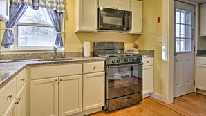 A kitchen with white cabinets, a stainless steel stove, a microwave, and a granite countertop. - Steps to Cape Cod Canal: Pet-friendly Home (Buzzards Bay)