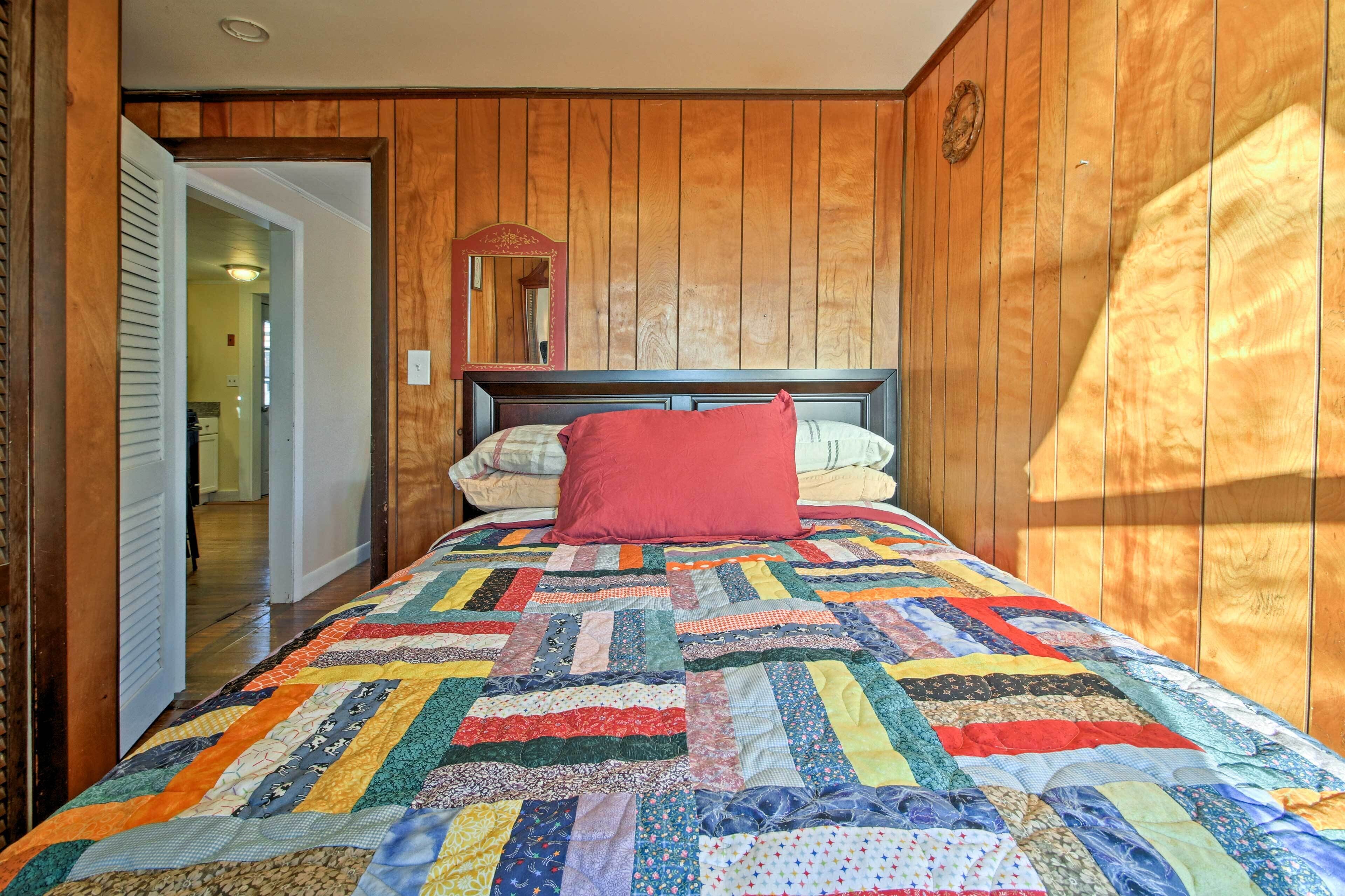 Un dormitorio con pared de paneles de madera, colcha acolchada y almohada roja.